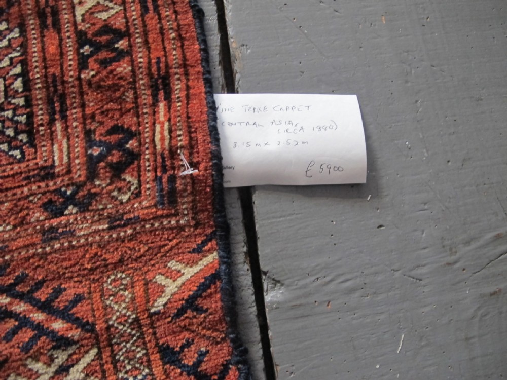 A large hand-knotted antique wool carpet featuring repeating octagonal Tekke gul motifs in rust red, cream, and navy blue with geometric borders. View XIV