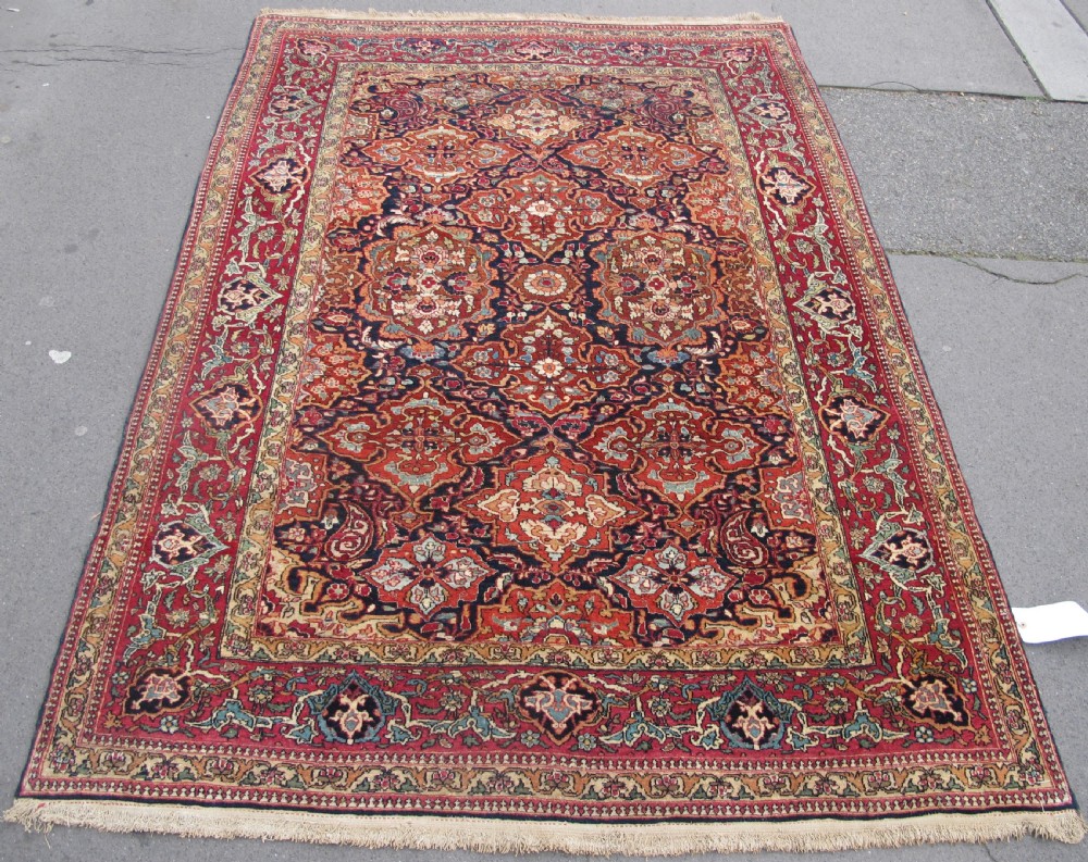 An antique hand-knotted Persian Isfahan rug featuring a dense floral lattice pattern in crimson red, navy blue, and cream with a detailed border.