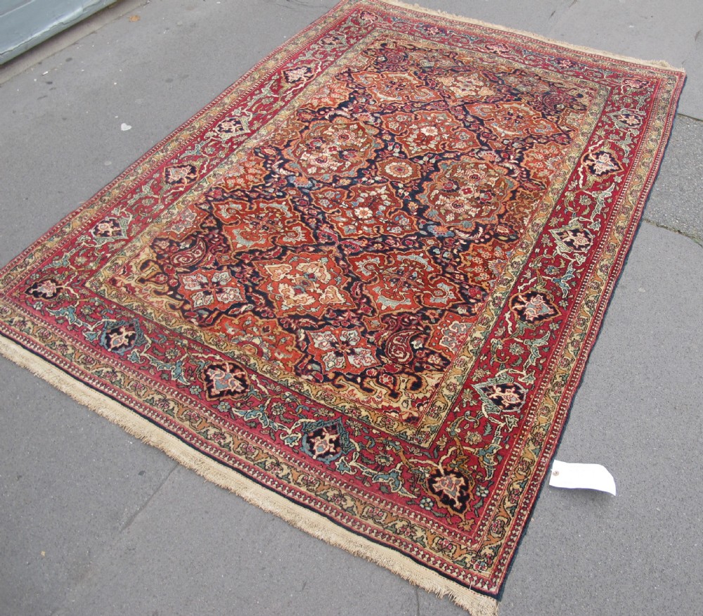 An antique hand-knotted Persian Isfahan rug featuring a dense floral lattice pattern in crimson red, navy blue, and cream with a detailed border. View III