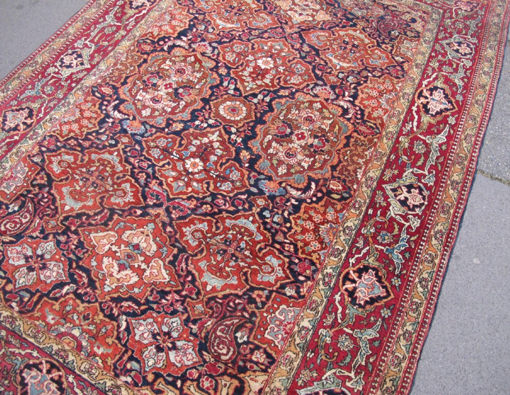 An antique hand-knotted Persian Isfahan rug featuring a dense floral lattice pattern in crimson red, navy blue, and cream with a detailed border. View V