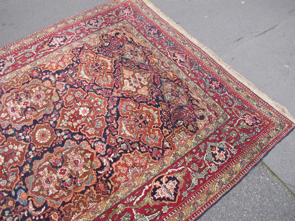 An antique hand-knotted Persian Isfahan rug featuring a dense floral lattice pattern in crimson red, navy blue, and cream with a detailed border. View VI