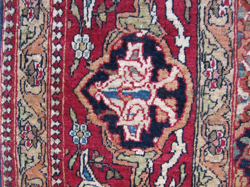 An antique hand-knotted Persian Isfahan rug featuring a dense floral lattice pattern in crimson red, navy blue, and cream with a detailed border. View VII