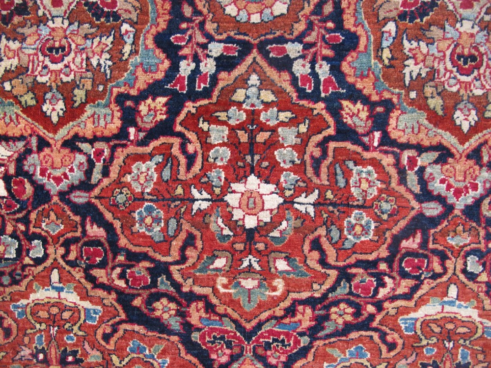 An antique hand-knotted Persian Isfahan rug featuring a dense floral lattice pattern in crimson red, navy blue, and cream with a detailed border. View VIII