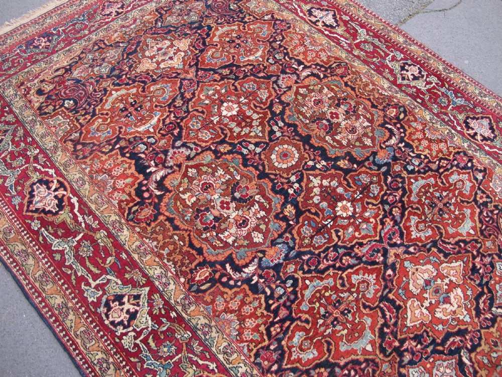An antique hand-knotted Persian Isfahan rug featuring a dense floral lattice pattern in crimson red, navy blue, and cream with a detailed border. View IX
