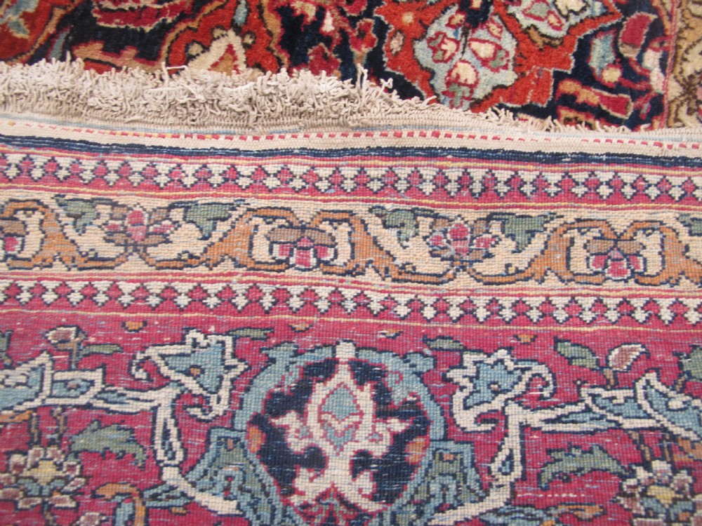 An antique hand-knotted Persian Isfahan rug featuring a dense floral lattice pattern in crimson red, navy blue, and cream with a detailed border. View X