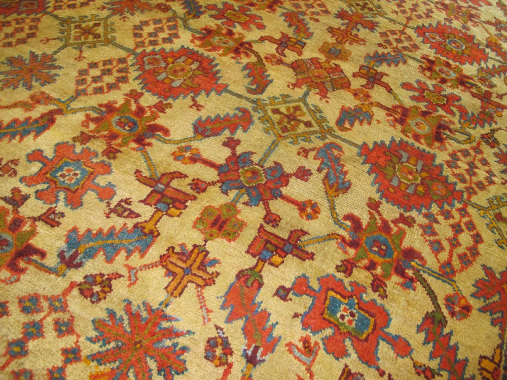 A large hand-knotted wool Oushak carpet featuring a golden-yellow field with geometric medallion motifs bordered by wide terracotta and orange patterned bands. View III