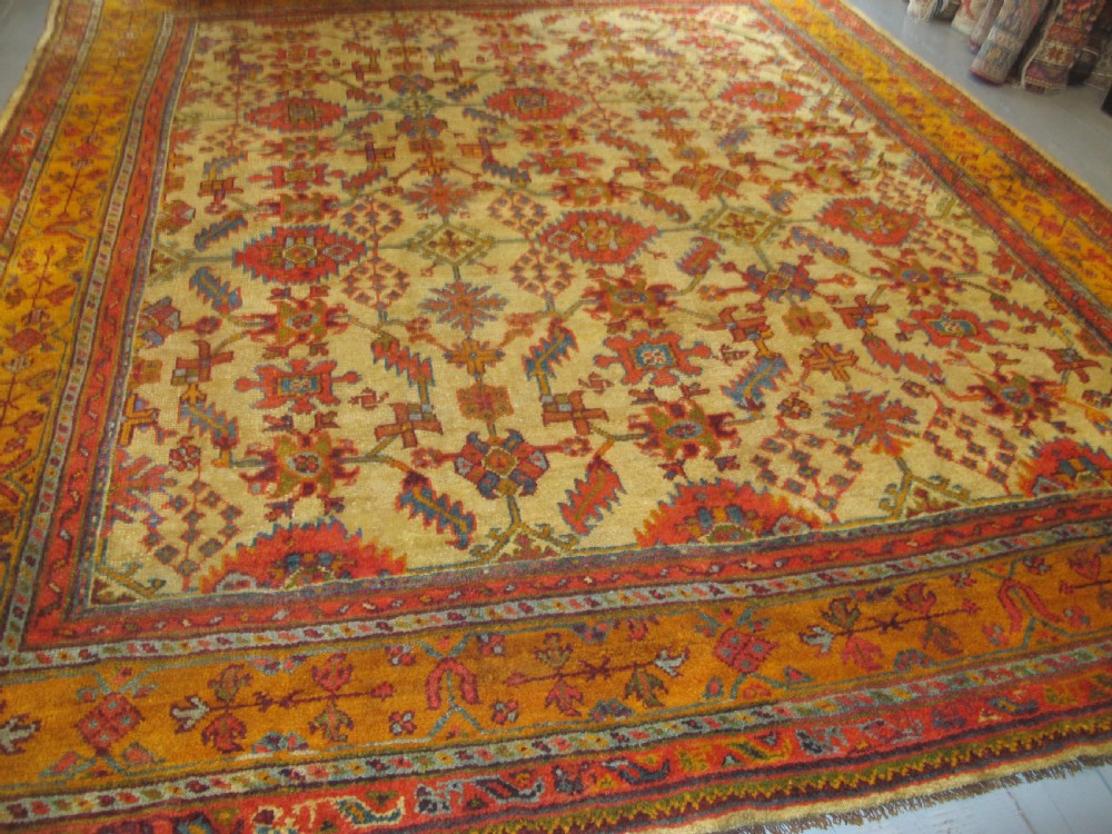 A large hand-knotted wool Oushak carpet featuring a golden-yellow field with geometric medallion motifs bordered by wide terracotta and orange patterned bands. View IV