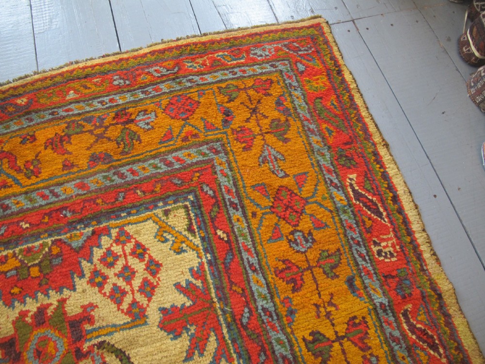 A large hand-knotted wool Oushak carpet featuring a golden-yellow field with geometric medallion motifs bordered by wide terracotta and orange patterned bands. View VII