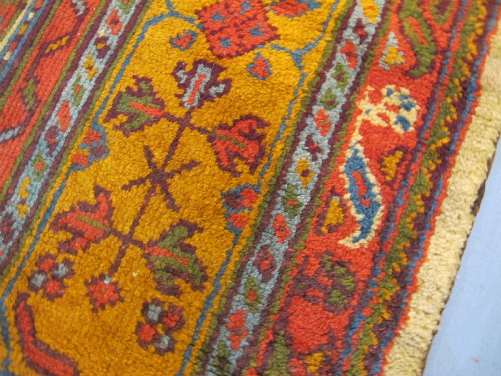A large hand-knotted wool Oushak carpet featuring a golden-yellow field with geometric medallion motifs bordered by wide terracotta and orange patterned bands. View X