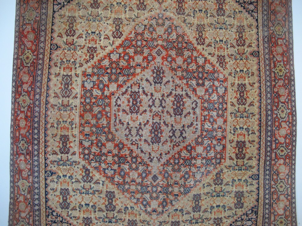 An antique Persian Senneh wool carpet featuring a large central diamond medallion surrounded by fine geometric patterning in terracotta, navy, and cream tones. View II