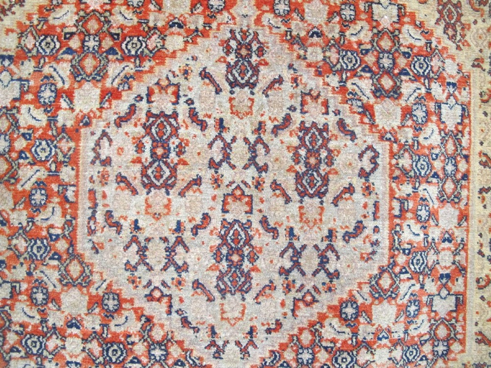 An antique Persian Senneh wool carpet featuring a large central diamond medallion surrounded by fine geometric patterning in terracotta, navy, and cream tones. View III