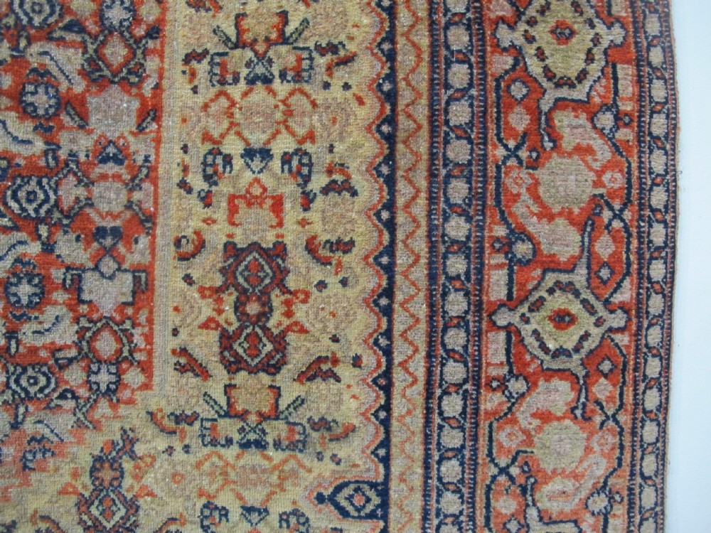 An antique Persian Senneh wool carpet featuring a large central diamond medallion surrounded by fine geometric patterning in terracotta, navy, and cream tones. View IV