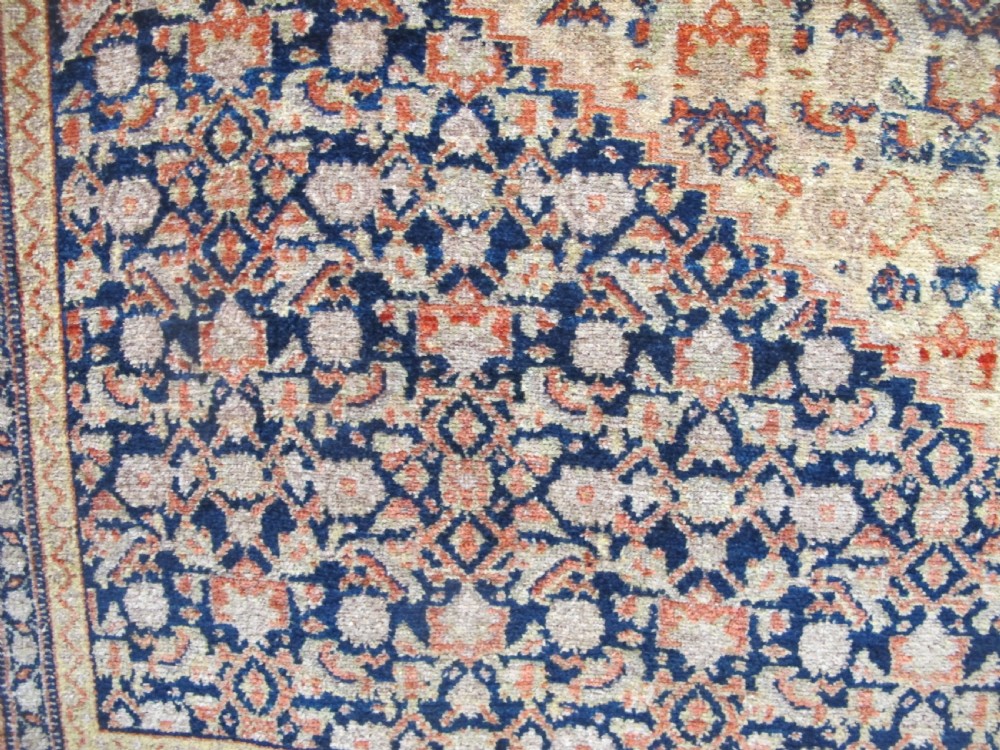 An antique Persian Senneh wool carpet featuring a large central diamond medallion surrounded by fine geometric patterning in terracotta, navy, and cream tones. View V