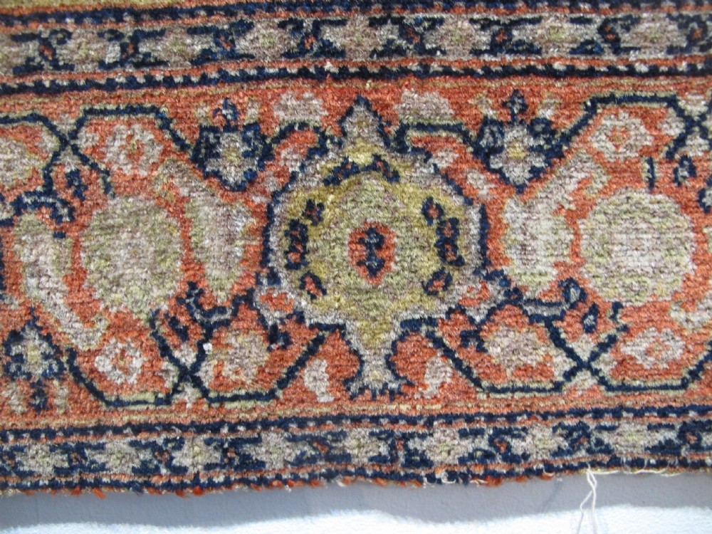 An antique Persian Senneh wool carpet featuring a large central diamond medallion surrounded by fine geometric patterning in terracotta, navy, and cream tones. View VI