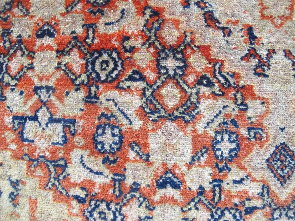 An antique Persian Senneh wool carpet featuring a large central diamond medallion surrounded by fine geometric patterning in terracotta, navy, and cream tones. View VII