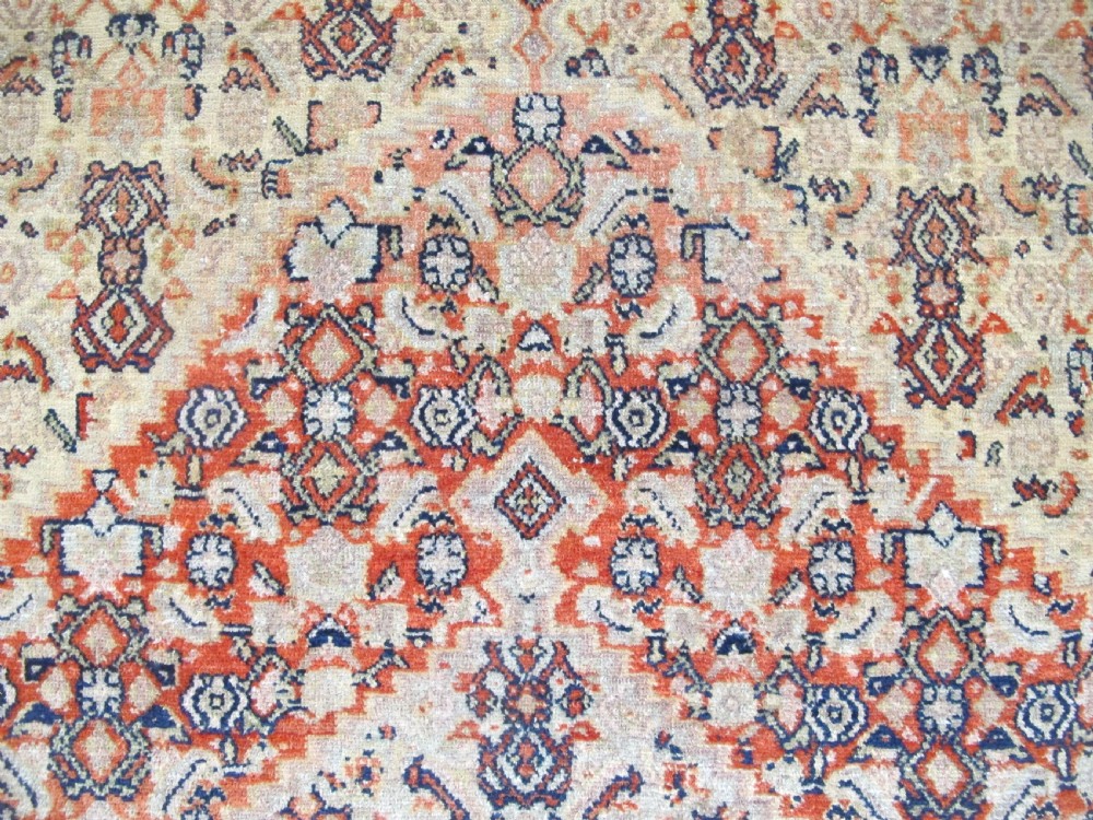 An antique Persian Senneh wool carpet featuring a large central diamond medallion surrounded by fine geometric patterning in terracotta, navy, and cream tones. View VIII