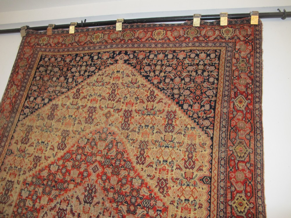 An antique Persian Senneh wool carpet featuring a large central diamond medallion surrounded by fine geometric patterning in terracotta, navy, and cream tones. View IX