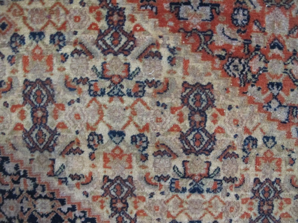 An antique Persian Senneh wool carpet featuring a large central diamond medallion surrounded by fine geometric patterning in terracotta, navy, and cream tones. View XI