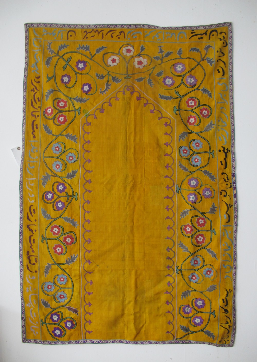 An early 20th-century yellow silk textile from Uzbekistan featuring hand-embroidered floral motifs, a central arch design, and calligraphic borders.