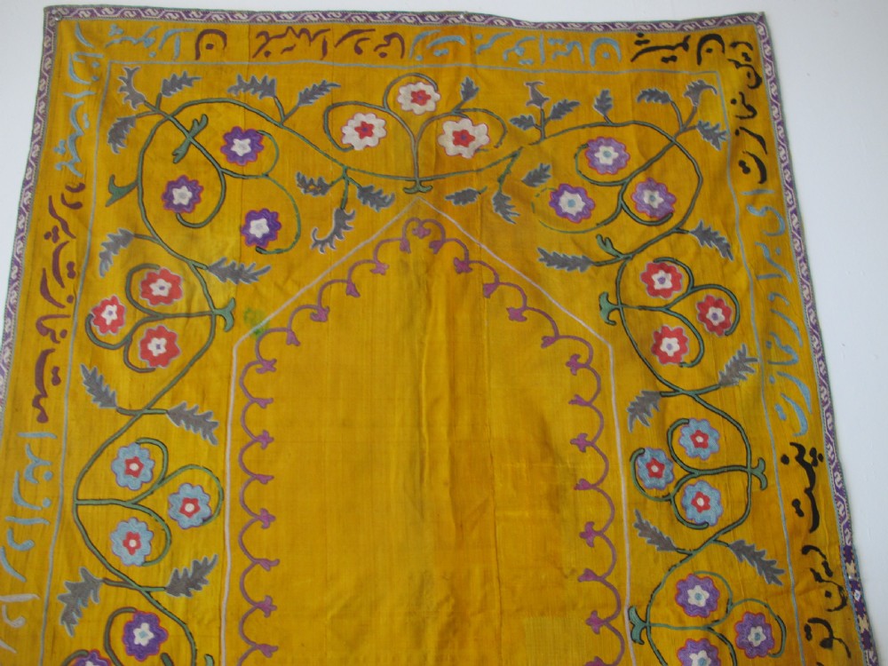 An early 20th-century yellow silk textile from Uzbekistan featuring hand-embroidered floral motifs, a central arch design, and calligraphic borders. View II