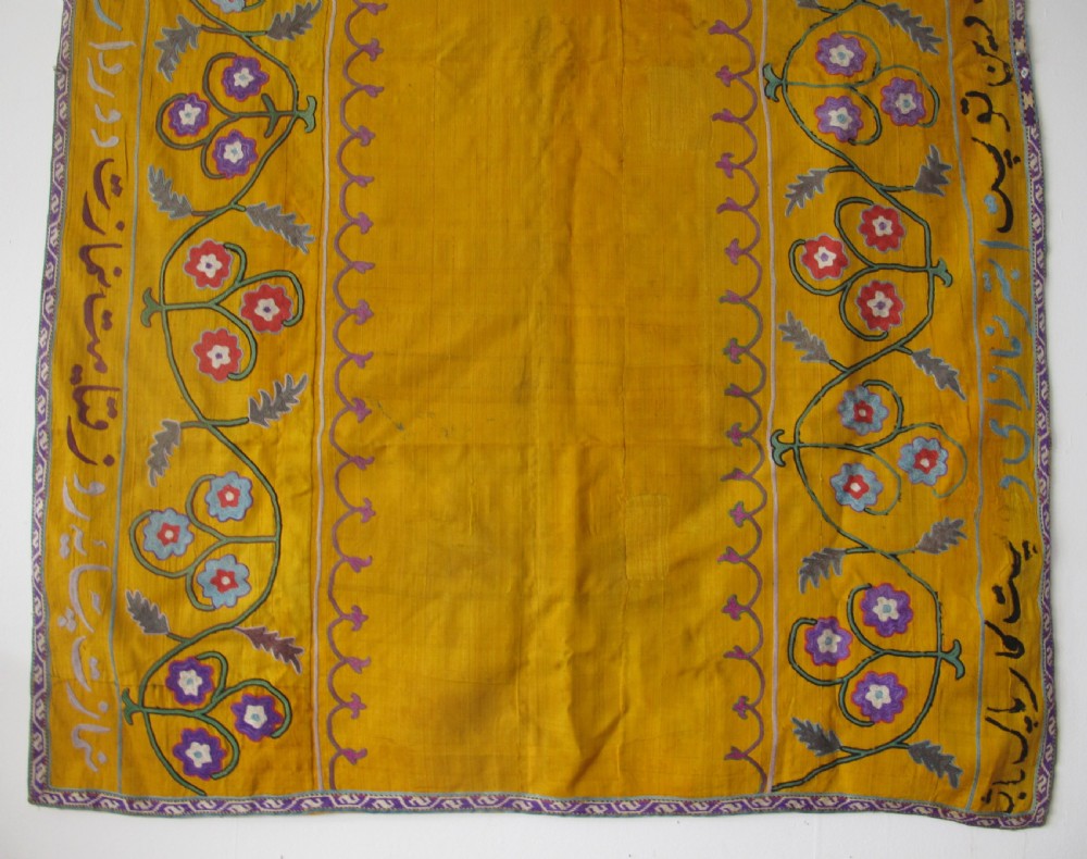 An early 20th-century yellow silk textile from Uzbekistan featuring hand-embroidered floral motifs, a central arch design, and calligraphic borders. View III