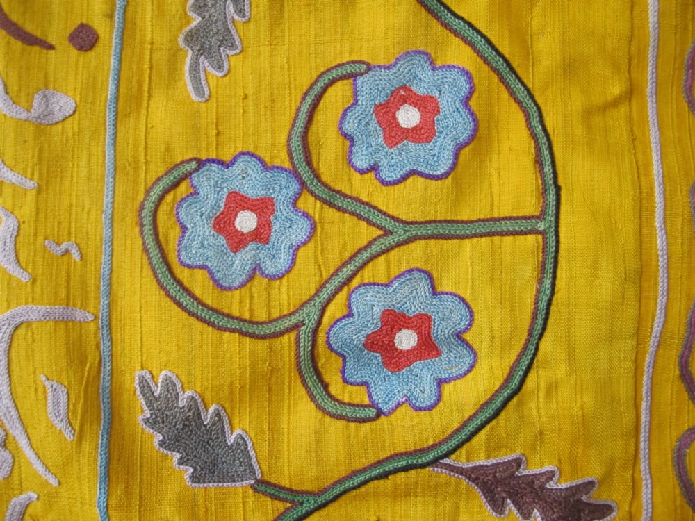 An early 20th-century yellow silk textile from Uzbekistan featuring hand-embroidered floral motifs, a central arch design, and calligraphic borders. View V