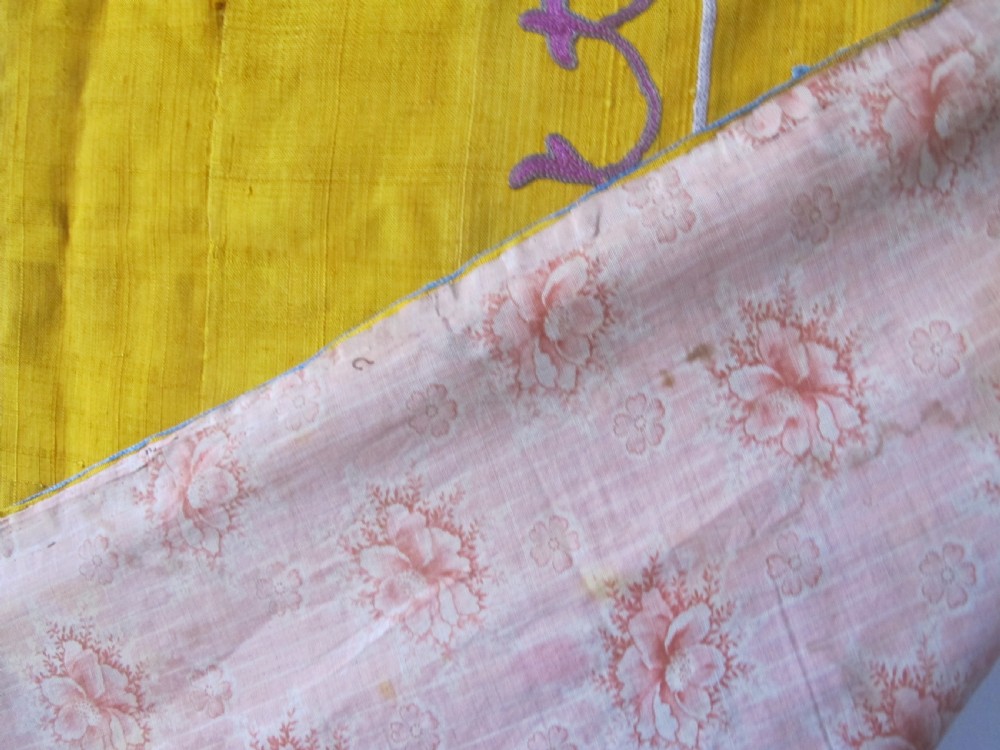 An early 20th-century yellow silk textile from Uzbekistan featuring hand-embroidered floral motifs, a central arch design, and calligraphic borders. View X