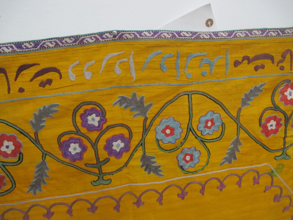 An early 20th-century yellow silk textile from Uzbekistan featuring hand-embroidered floral motifs, a central arch design, and calligraphic borders. View XII