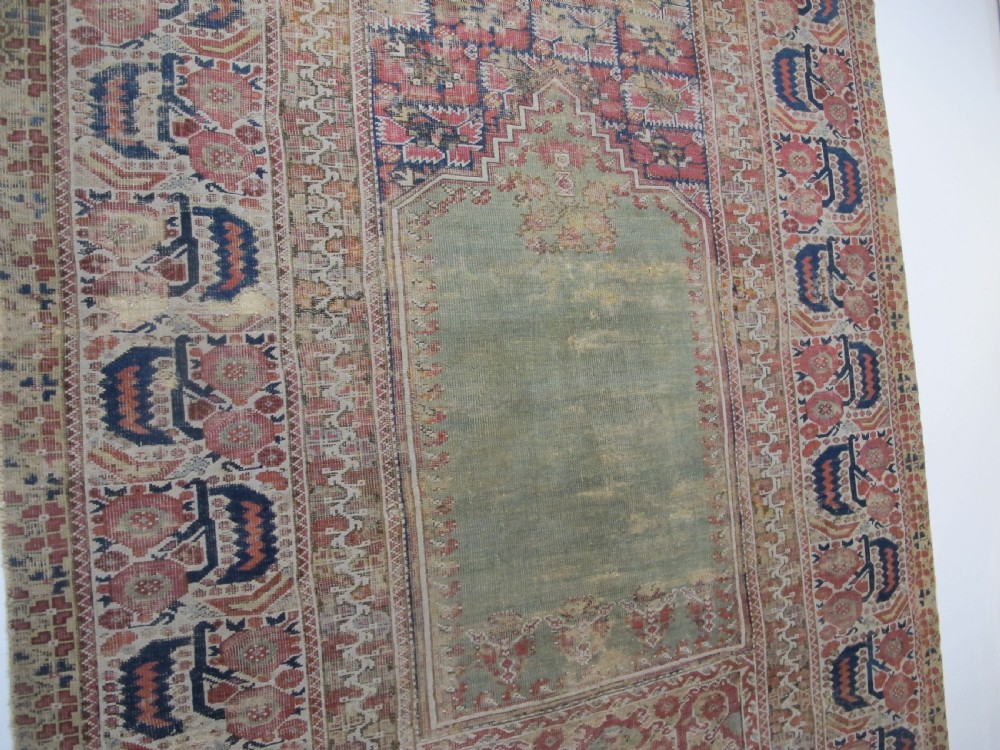 An 18th-century hand-knotted Ghiordes prayer rug featuring a central pale green mihrab niche framed by intricate floral borders in red, blue, and beige. View IX