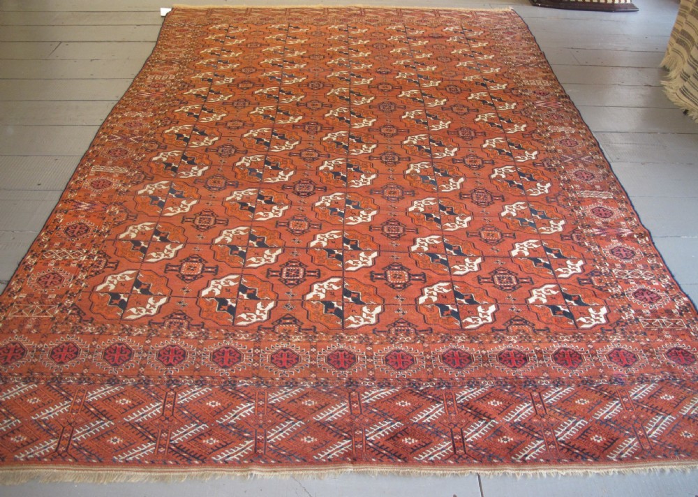 An antique hand-knotted Central Asian wool carpet featuring repeating rows of octagonal gol motifs on a terracotta red ground with detailed borders.