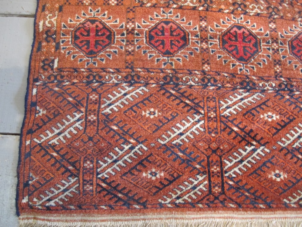 An antique hand-knotted Central Asian wool carpet featuring repeating rows of octagonal gol motifs on a terracotta red ground with detailed borders. View III