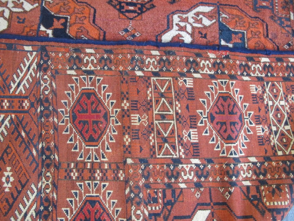 An antique hand-knotted Central Asian wool carpet featuring repeating rows of octagonal gol motifs on a terracotta red ground with detailed borders. View IV