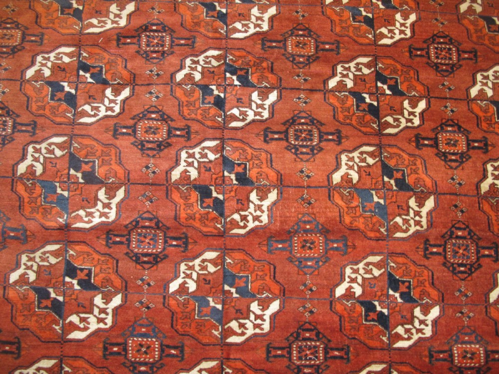 An antique hand-knotted Central Asian wool carpet featuring repeating rows of octagonal gol motifs on a terracotta red ground with detailed borders. View V