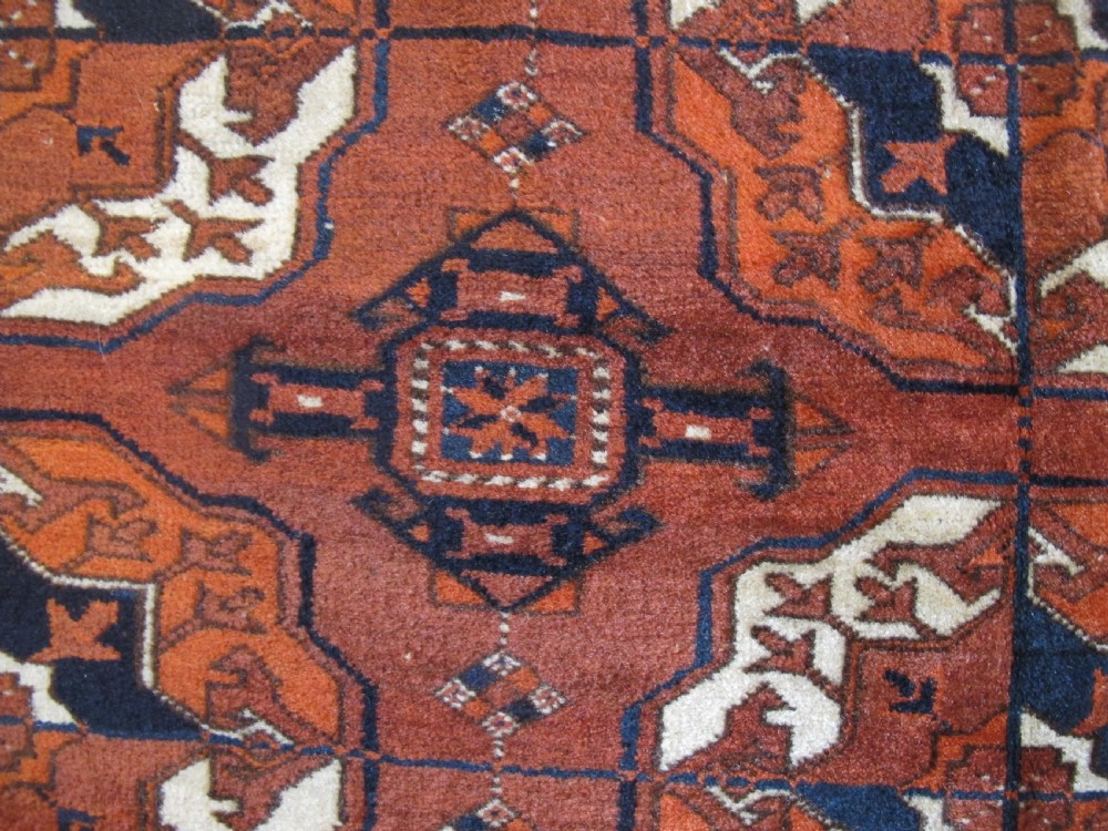 An antique hand-knotted Central Asian wool carpet featuring repeating rows of octagonal gol motifs on a terracotta red ground with detailed borders. View VIII