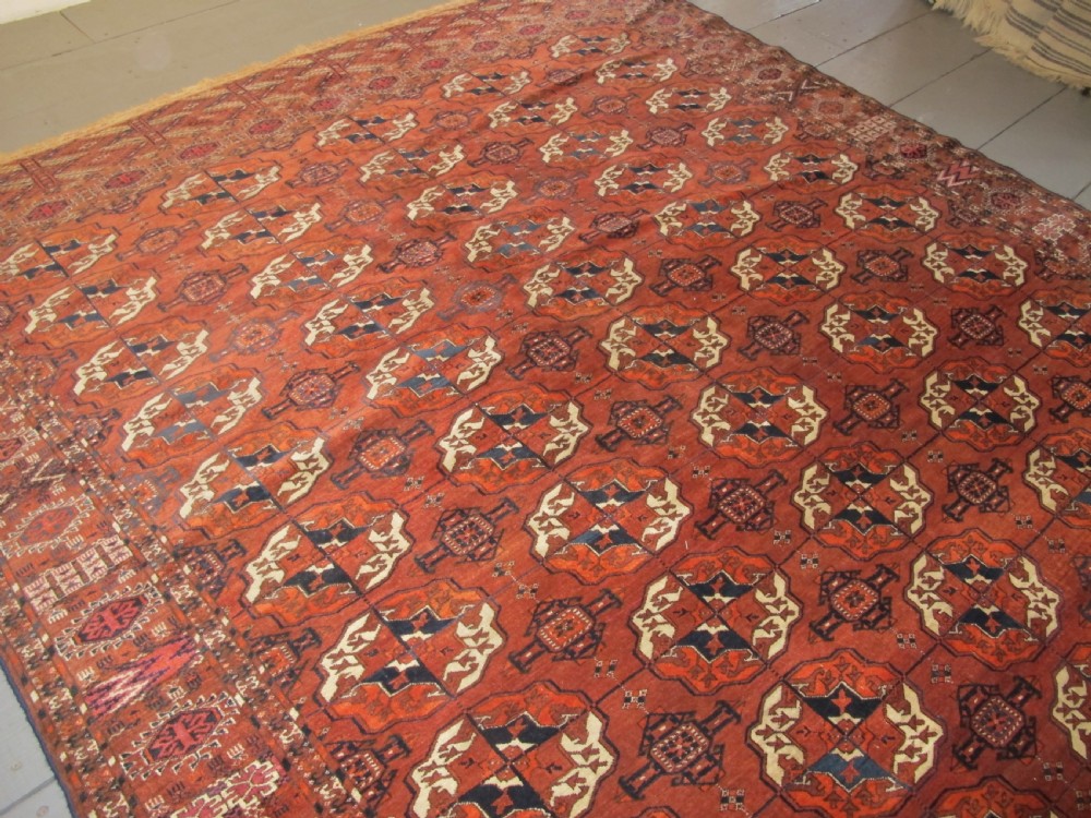 An antique hand-knotted Central Asian wool carpet featuring repeating rows of octagonal gol motifs on a terracotta red ground with detailed borders. View IX