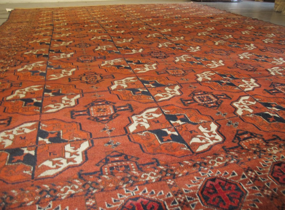 An antique hand-knotted Central Asian wool carpet featuring repeating rows of octagonal gol motifs on a terracotta red ground with detailed borders. View X
