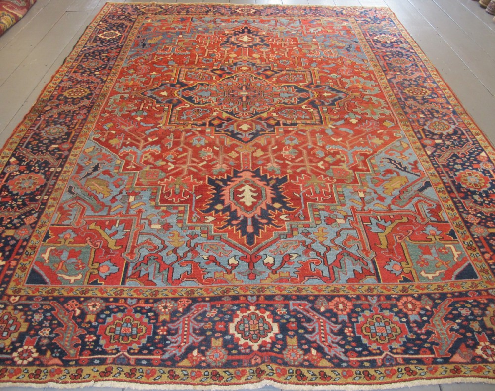 An antique Persian Karaja wool carpet featuring a large central geometric medallion surrounded by intricate red, blue, and light blue geometric borders.