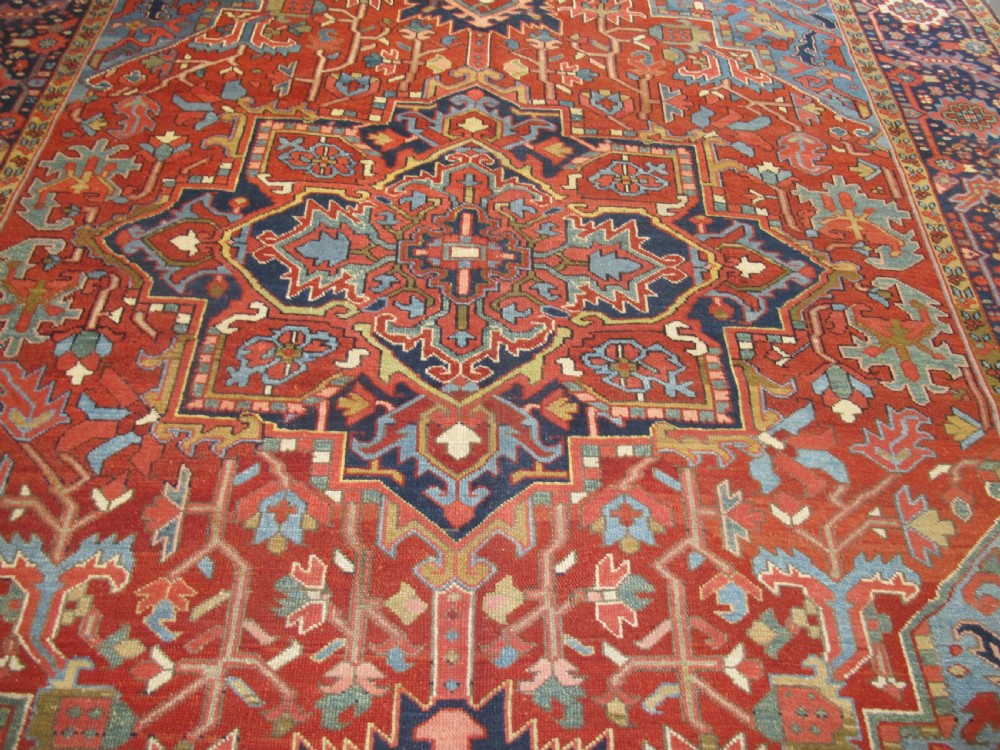 An antique Persian Karaja wool carpet featuring a large central geometric medallion surrounded by intricate red, blue, and light blue geometric borders. View II