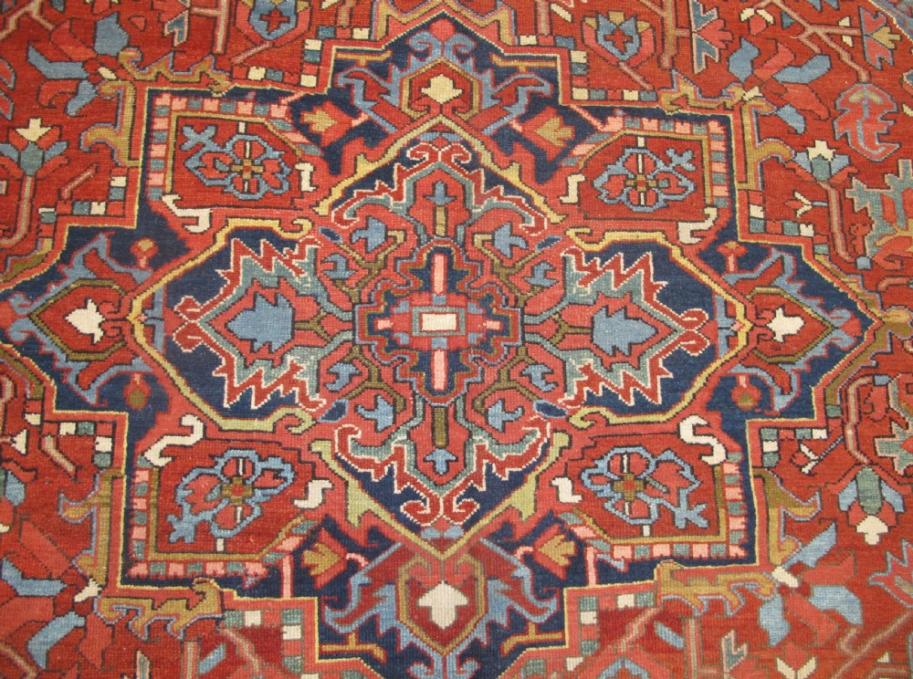 An antique Persian Karaja wool carpet featuring a large central geometric medallion surrounded by intricate red, blue, and light blue geometric borders. View III