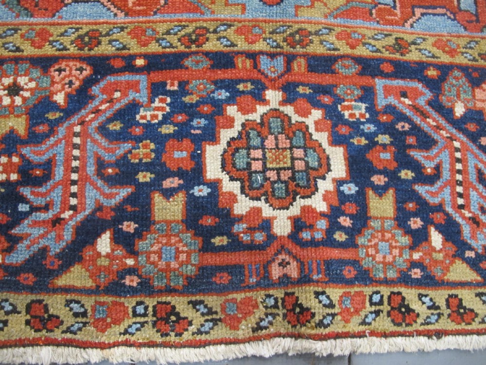 An antique Persian Karaja wool carpet featuring a large central geometric medallion surrounded by intricate red, blue, and light blue geometric borders. View IV