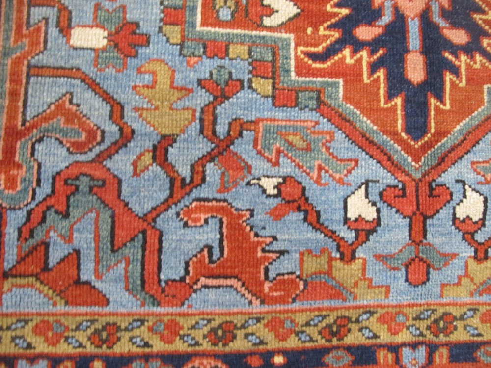An antique Persian Karaja wool carpet featuring a large central geometric medallion surrounded by intricate red, blue, and light blue geometric borders. View VI