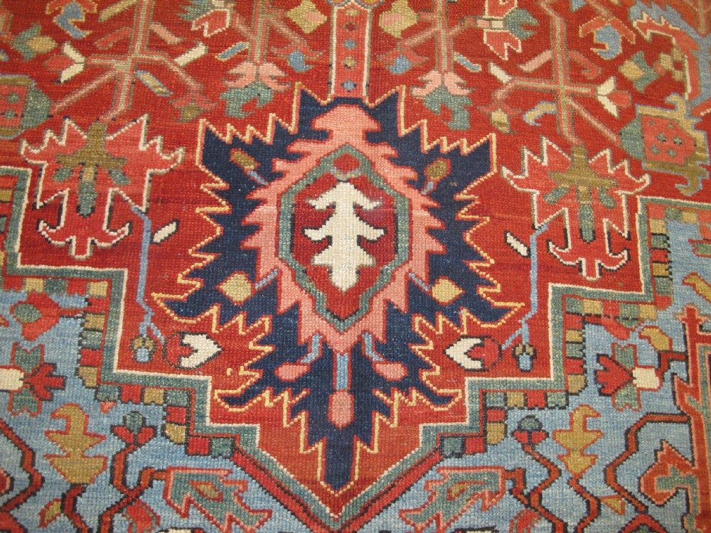 An antique Persian Karaja wool carpet featuring a large central geometric medallion surrounded by intricate red, blue, and light blue geometric borders. View VII