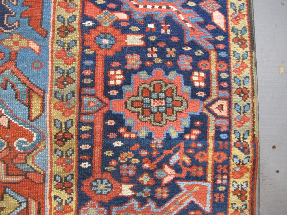 An antique Persian Karaja wool carpet featuring a large central geometric medallion surrounded by intricate red, blue, and light blue geometric borders. View IX