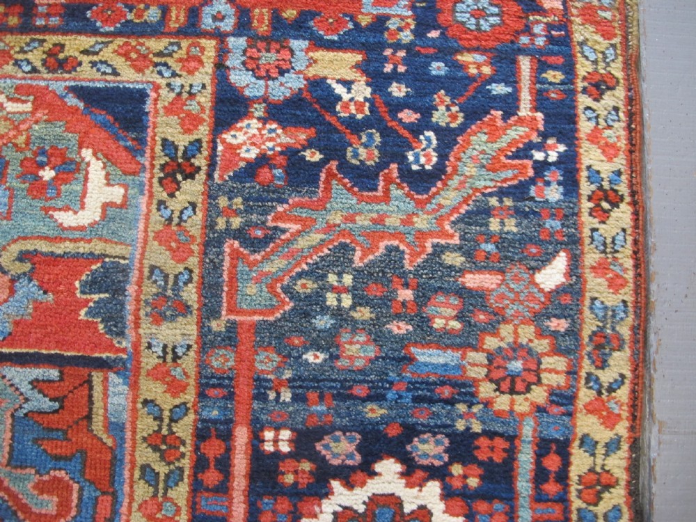 An antique Persian Karaja wool carpet featuring a large central geometric medallion surrounded by intricate red, blue, and light blue geometric borders. View X