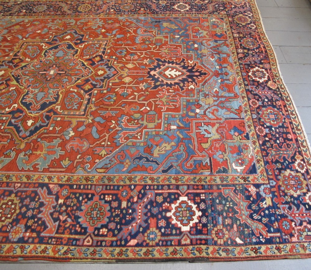 An antique Persian Karaja wool carpet featuring a large central geometric medallion surrounded by intricate red, blue, and light blue geometric borders. View XII