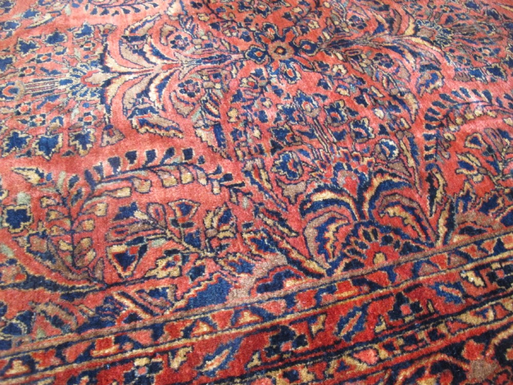 A large hand-knotted Persian Sarouk carpet featuring a dense floral pattern on a rose red field with a navy blue border. View II