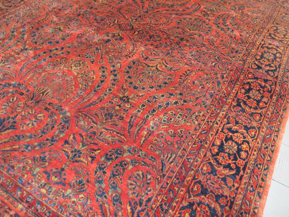 A large hand-knotted Persian Sarouk carpet featuring a dense floral pattern on a rose red field with a navy blue border. View IV