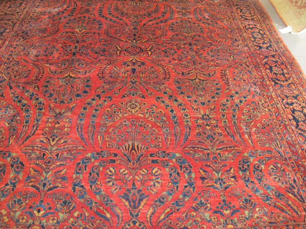 A large hand-knotted Persian Sarouk carpet featuring a dense floral pattern on a rose red field with a navy blue border. View V