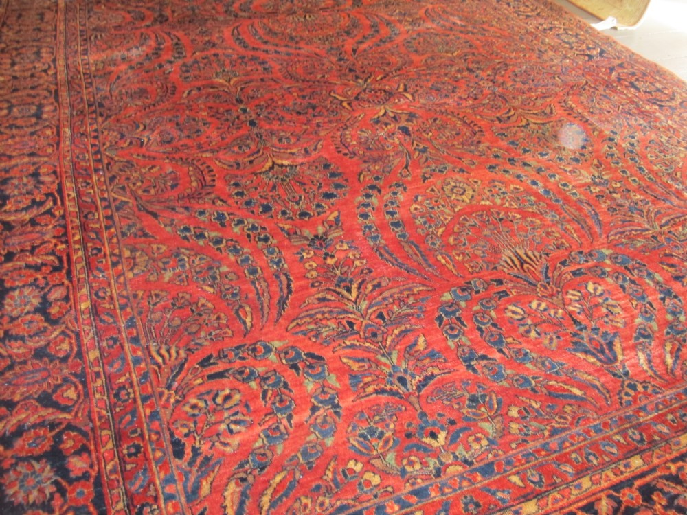 A large hand-knotted Persian Sarouk carpet featuring a dense floral pattern on a rose red field with a navy blue border. View VI