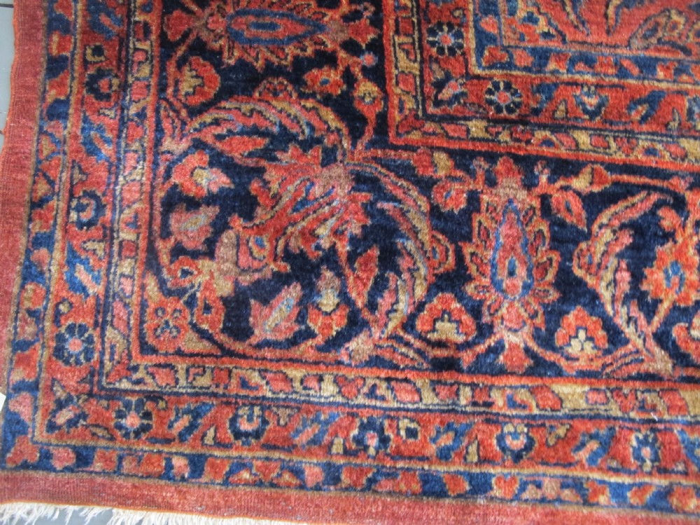 A large hand-knotted Persian Sarouk carpet featuring a dense floral pattern on a rose red field with a navy blue border. View VII